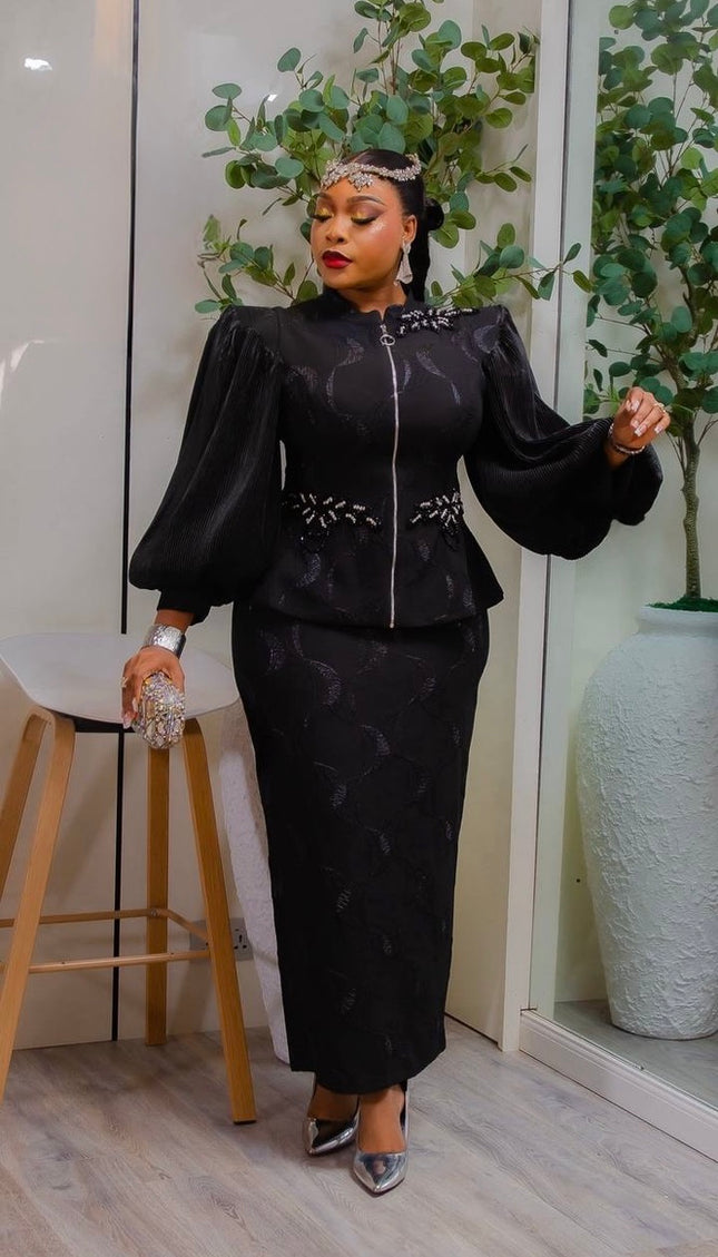 Woman in a black outfit with floral details standing indoors with plants in the background