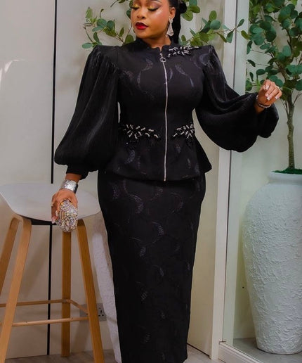 Woman in a black outfit with floral details standing indoors with plants in the background