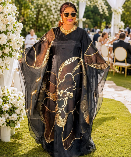Woman in a black and gold dress at an outdoor event with floral decorations.